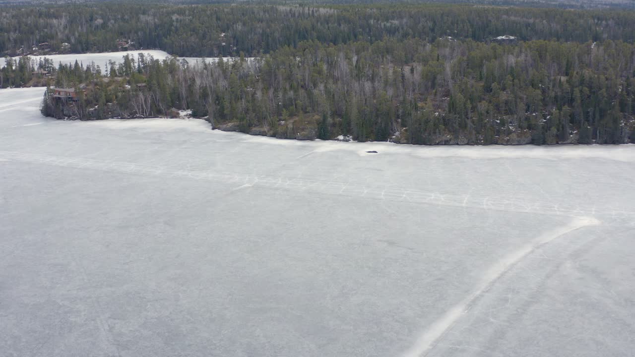 Aerial dolly left over melting frozen lake with cracks in the ice roads still visible in Canada