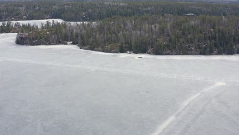 aerial dolly left over melting frozen lake with cracks in the ice roads still visible in canada