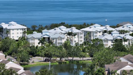 aerial view of coastal florida condos surrounded by palm trees, water and lush greenery on a sunny day. typical american seaside residential lifestyle. wide shot. cortez, florida. noble district.