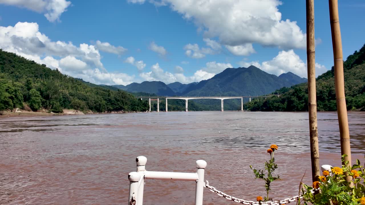 Stævnen på en langsom båd, der sejler på Mekong-floden med en højhastighedsjernbanebro i baggrunden