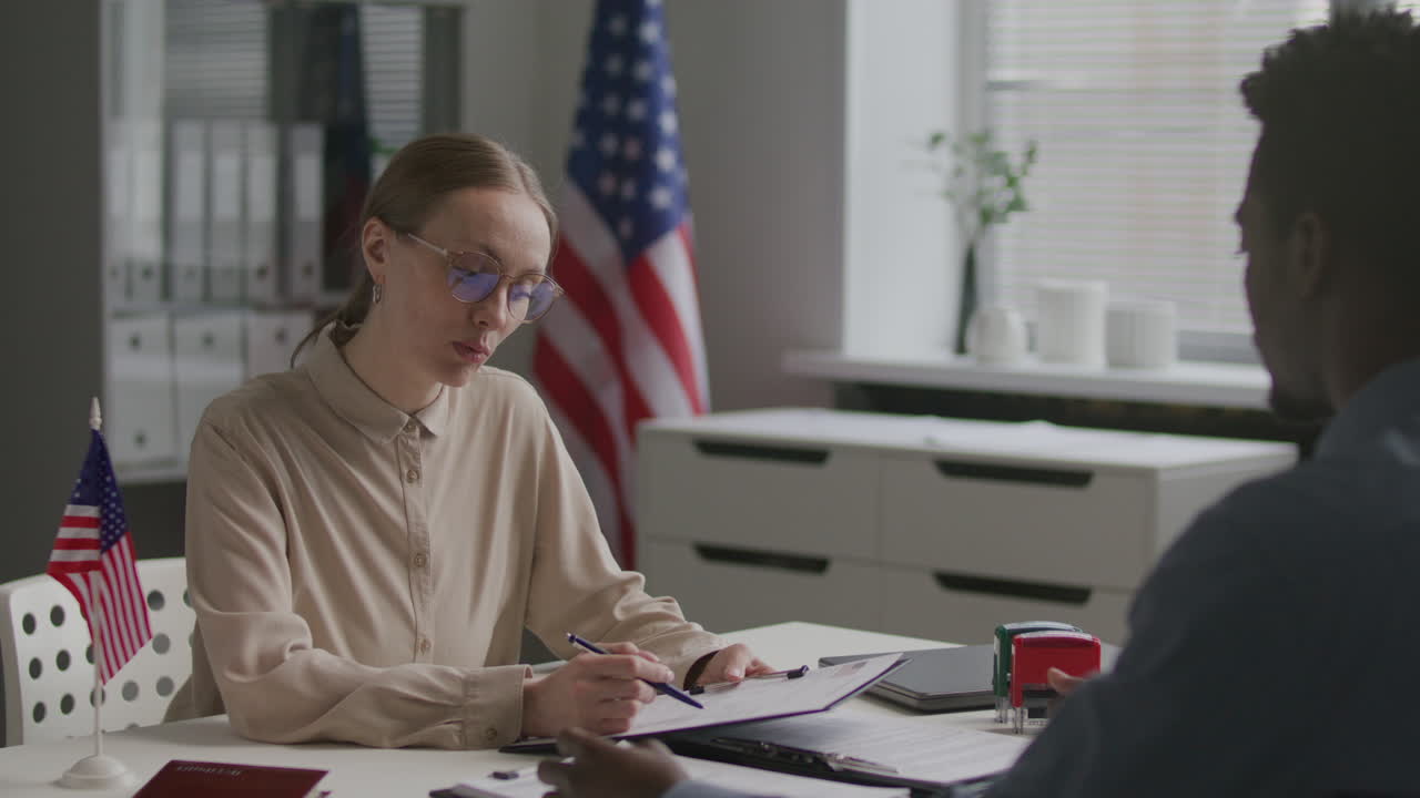 Visa Officer Reading Application Form and Interviewing Black Man at US Embassy