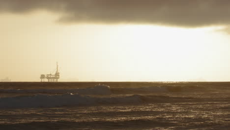 slow motion waves crashing with an oil rig in the background at sunset