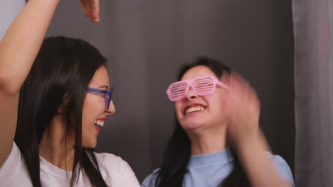 two female friends in photo booth wearing cool glasses having fun posing for portrait and pulling faces in real time 1