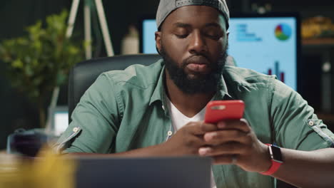 Focused-african-american-man-typing-message-on-mobile-phone-in-modern-office