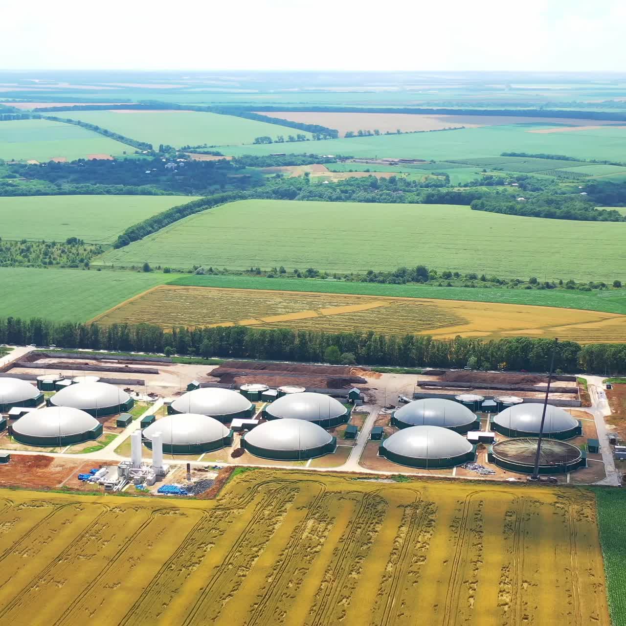 Flight over biogas power plants. Aerial view of big biogas plant between green agricultural fields