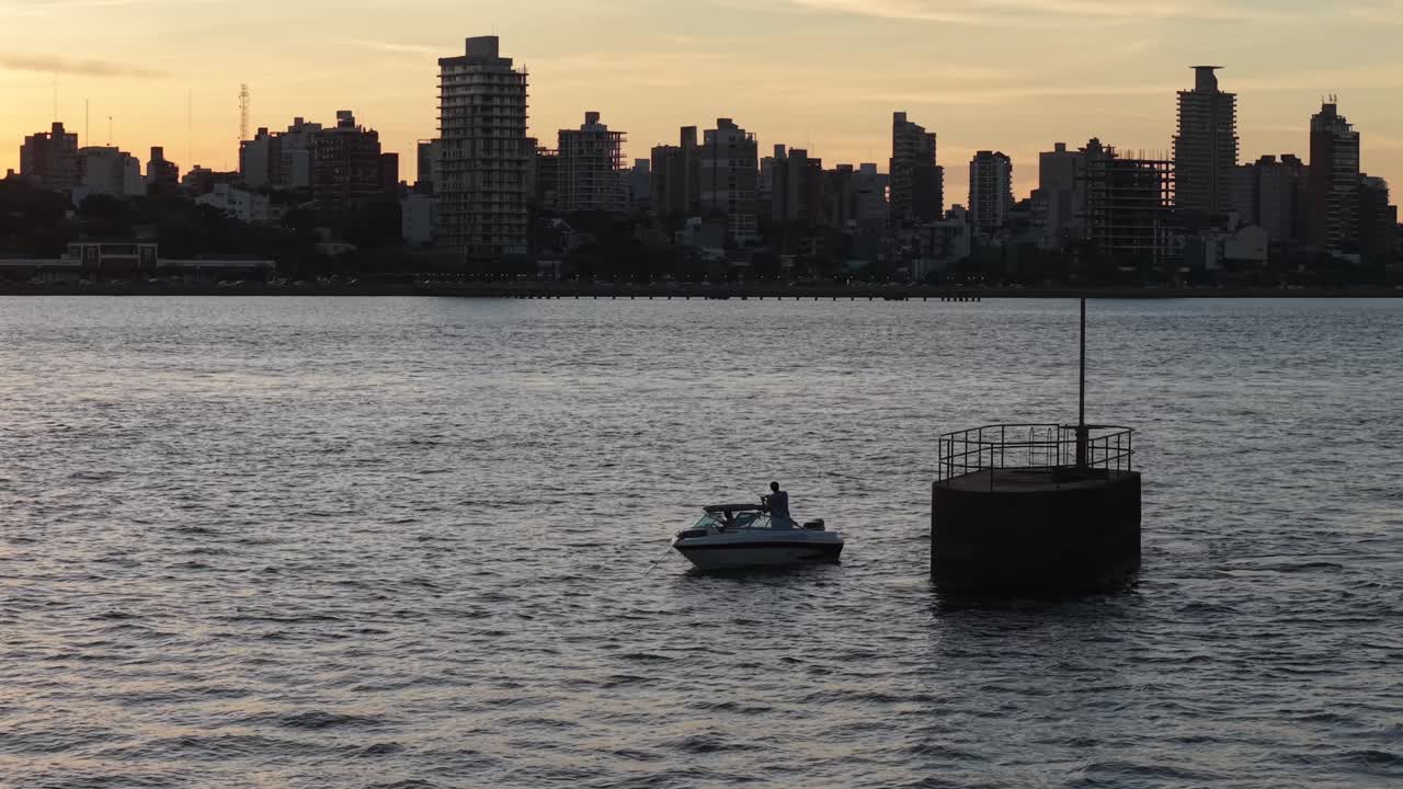 Fishing boat floats on Parana River at sunset with Posadas skyline in background