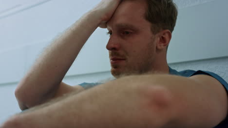 upset doctor holding hand on face sitting floor hospital corridor closeup.