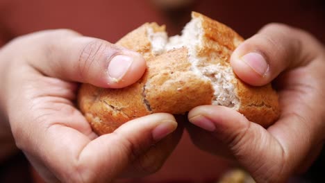 person breaking a loaf of bread in half