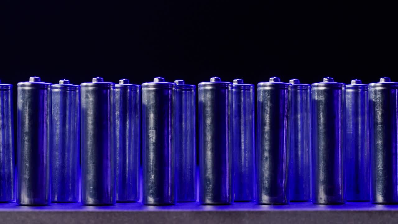 Silver batteries AA and AAA in neon light close-up. Double-A battery is a standard size single cell cylindrical dry battery. Batteries are common in portable electronic devices. An AA battery is composed of a single electrochemical cell that may be either a primary battery or a rechargeable battery.