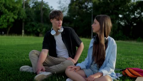 a boy and girl sitting in the grass talking to each other