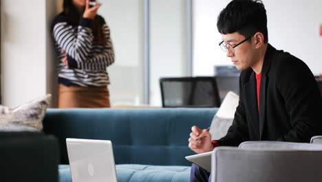 Side-view-of-Asian-Businessman-working-on-laptop-and-writing-on-notepad-in-modern-office-4k