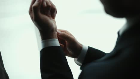 confident businessman in classic blue suit buttoning or adjust cufflinks near window in hotel room at the morning. handsome man wearing a nice suit on wedding day.