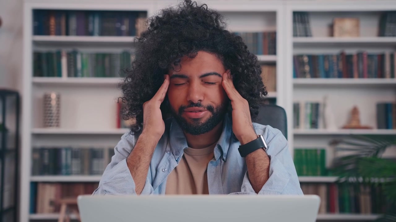 Exhausted Young Man Suffering from Headache While Working on Laptop