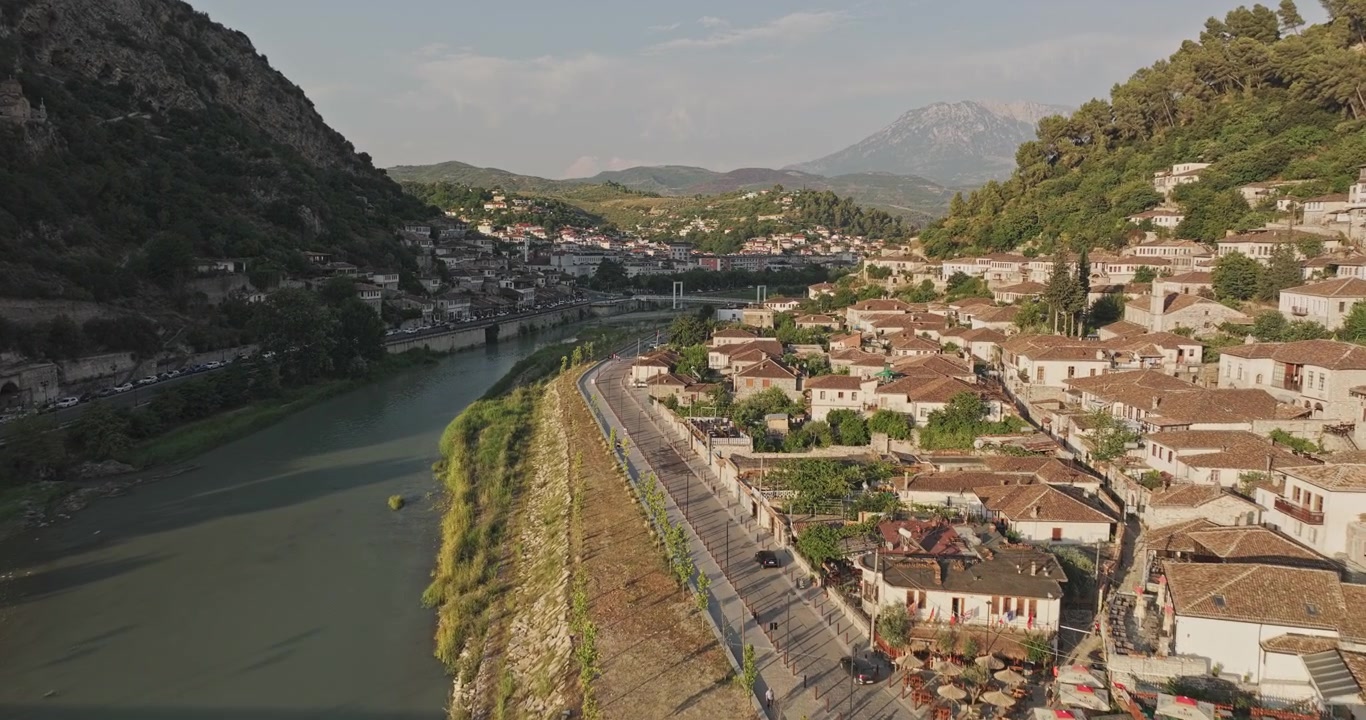 Berat Albania Aerial v12 low flyover along the Osum River and Gorica, capturing traditional hillside homes, a pedestrian bridge and mountains at sunset - Shot with Mavic 3 Pro Cine - July 11th 2024
