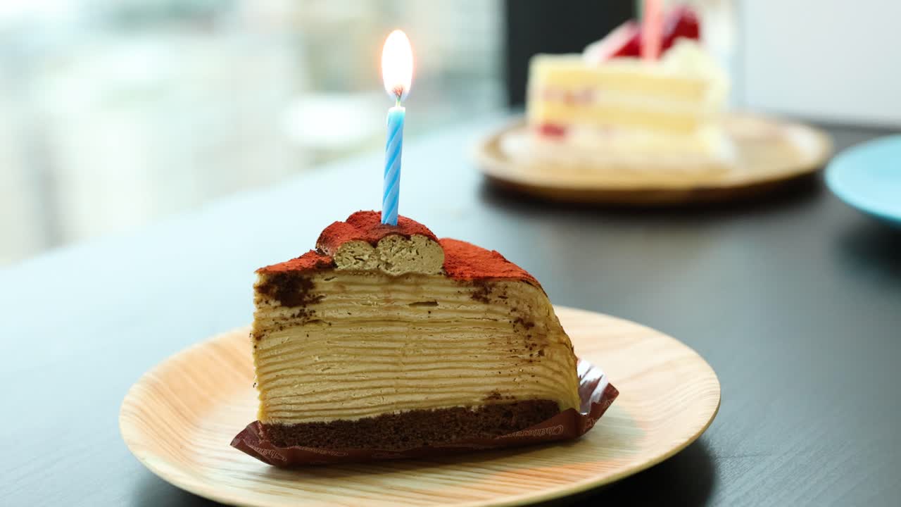 Tiramisu crepe cake slice with blue candle burning, natural daylight, shallow depth of field