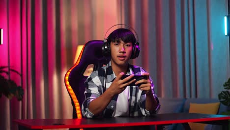 asian teen boy gamer smiling to camera while playing video game on smartphone