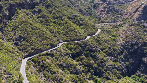 scenic mountain pass road along steep slope during sunny day, aerial