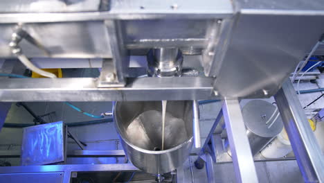 thick creamy condensed milk being poured from a pipe into a metal tank. confectionery production line at food factory.