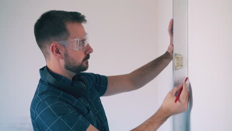 builder-in-shirt-uses-level-to-check-wall-angle-in-room