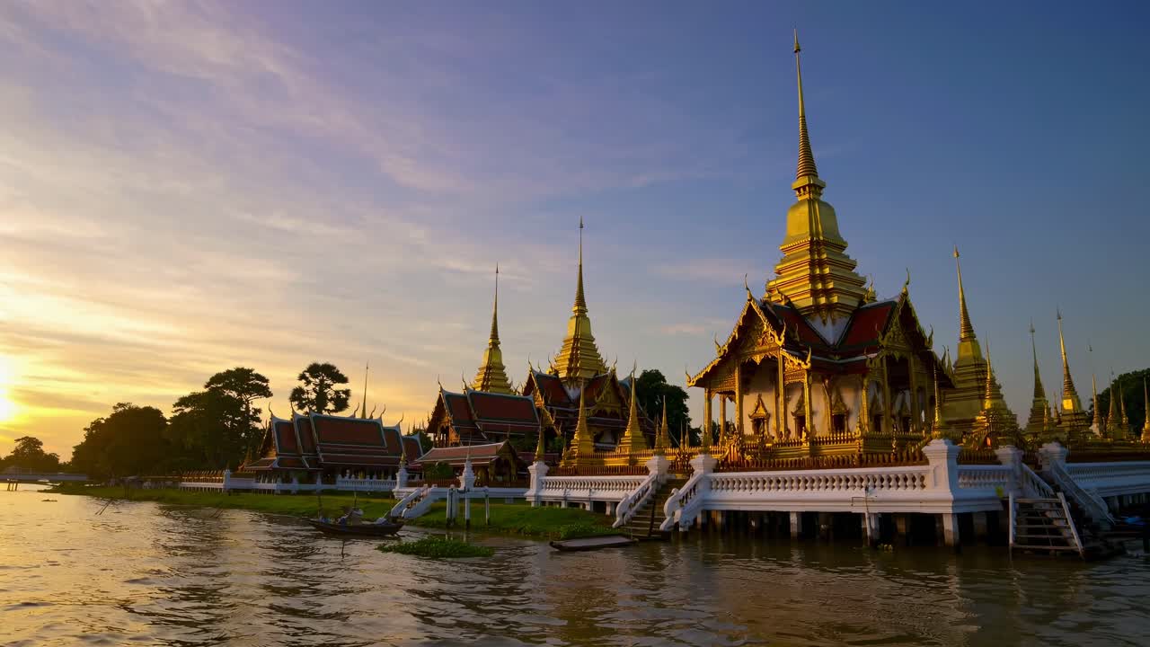 Foto grandangolare di un tempio thailandese vicino a un fiume al tramonto, che cattura guglie dorate e riflessi