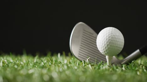 Close-up-of-golf-club-and-ball-on-grass-and-black-background,-copy-space,-slow-motion