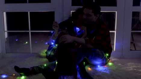 una pareja enamorada se sienta en el suelo cerca de la ventana y juega con el perro.