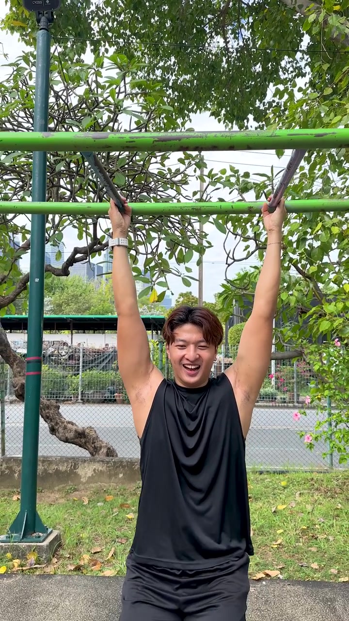 Fit young man in a black tank top performs pull-ups at an outdoor gym
