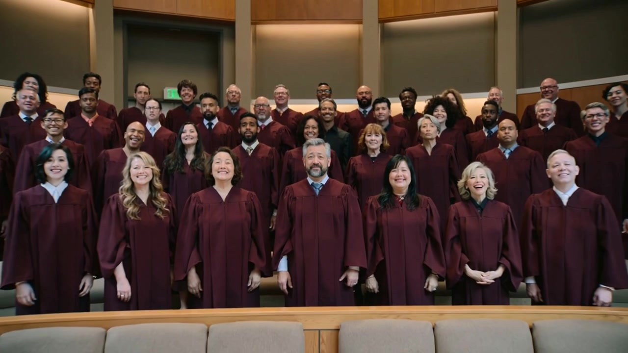 La telecamera si allontana, un coro sorridente si sistema dopo una frase musicale sulle pedane della chiesa, indossando tuniche bordeaux.