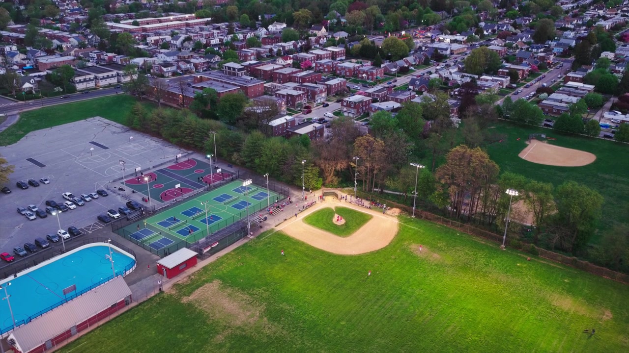 Vista aerea da drone al tramonto di un complesso ricreativo di Philadelphia con campi da baseball, campi da tennis, una piscina e il quartiere residenziale circostante sottostante