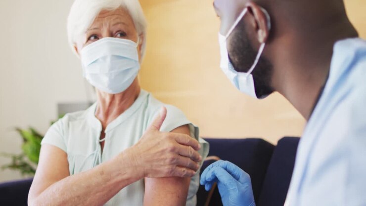 Video of african american male doctor in face mask vaccinating caucasian senior woman