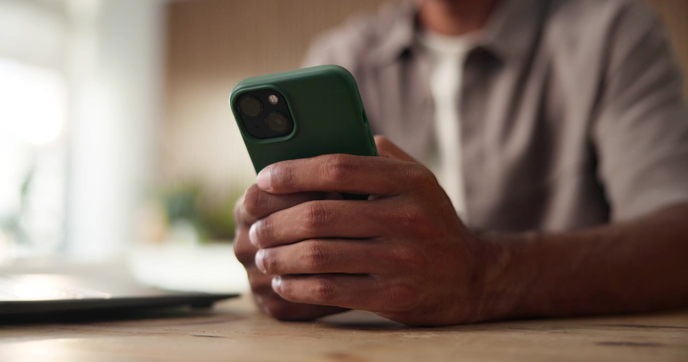 Mand der holder og bruger en smartphone ved et skrivebord