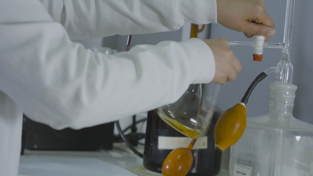 Medium shot of a laboratory scene with a flask and burette containing moving liquids.
