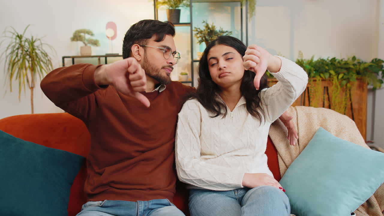 Upset indian couple showing thumbs down gesture expressing discontent disapproval dissatisfied