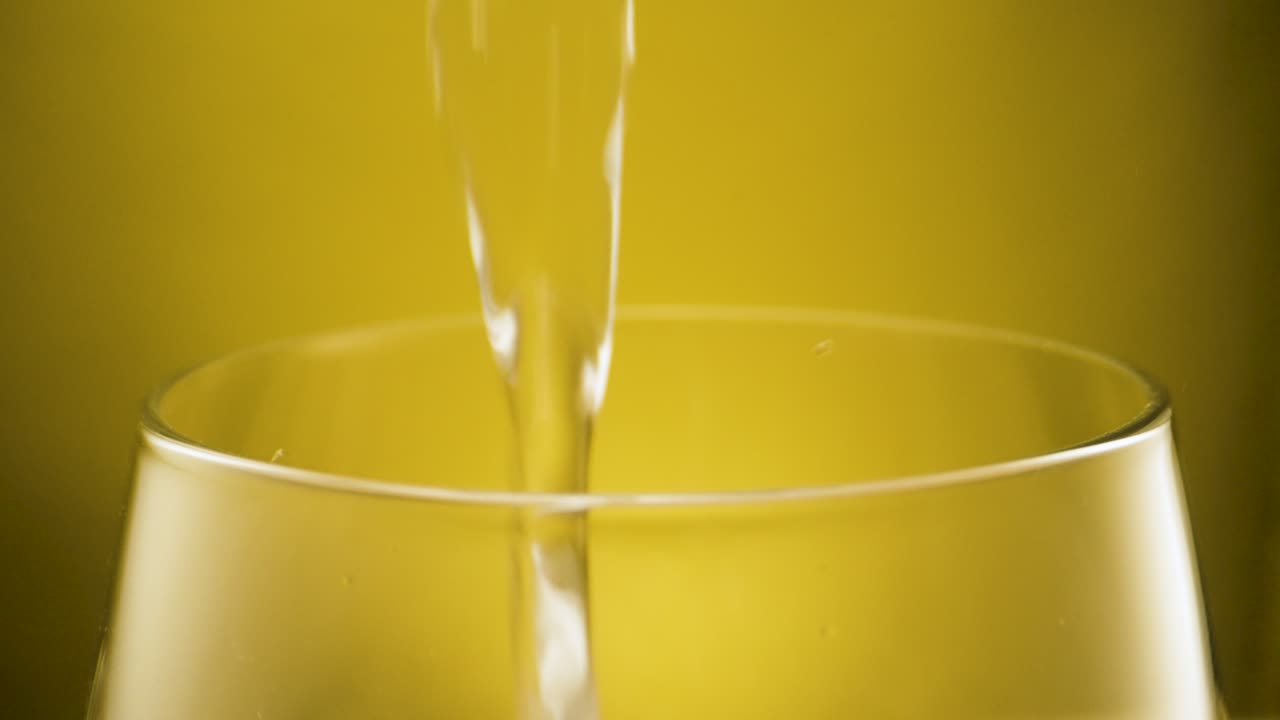 Primo piano: versamento di acqua potabile fresca e limpida in un bicchiere trasparente, sfondo giallo