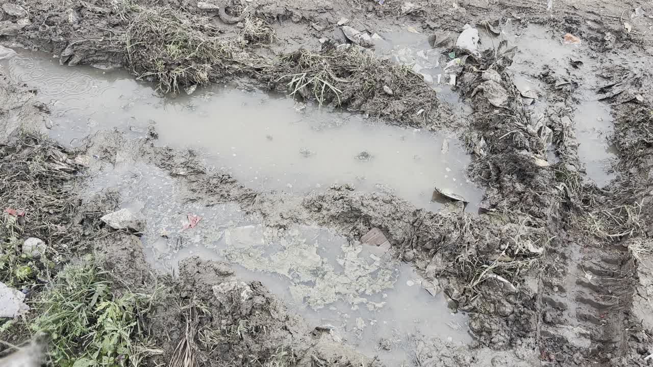 Close-up of muddy ground with stagnant rainwater and tire marks beside a highway in India, showing monsoon waterlogging and poor drainage