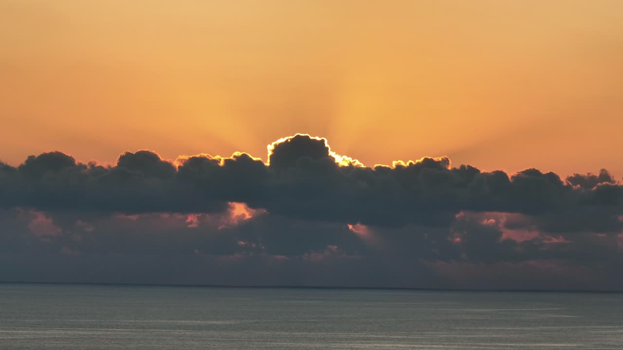 sol naranja estallando a través de las nubes durante un hermoso amanecer sobre el mar tranquilo