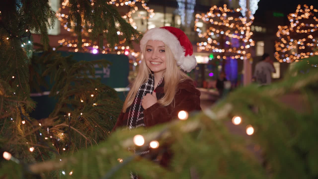 young attractive lady stands under xmas tree and smiles