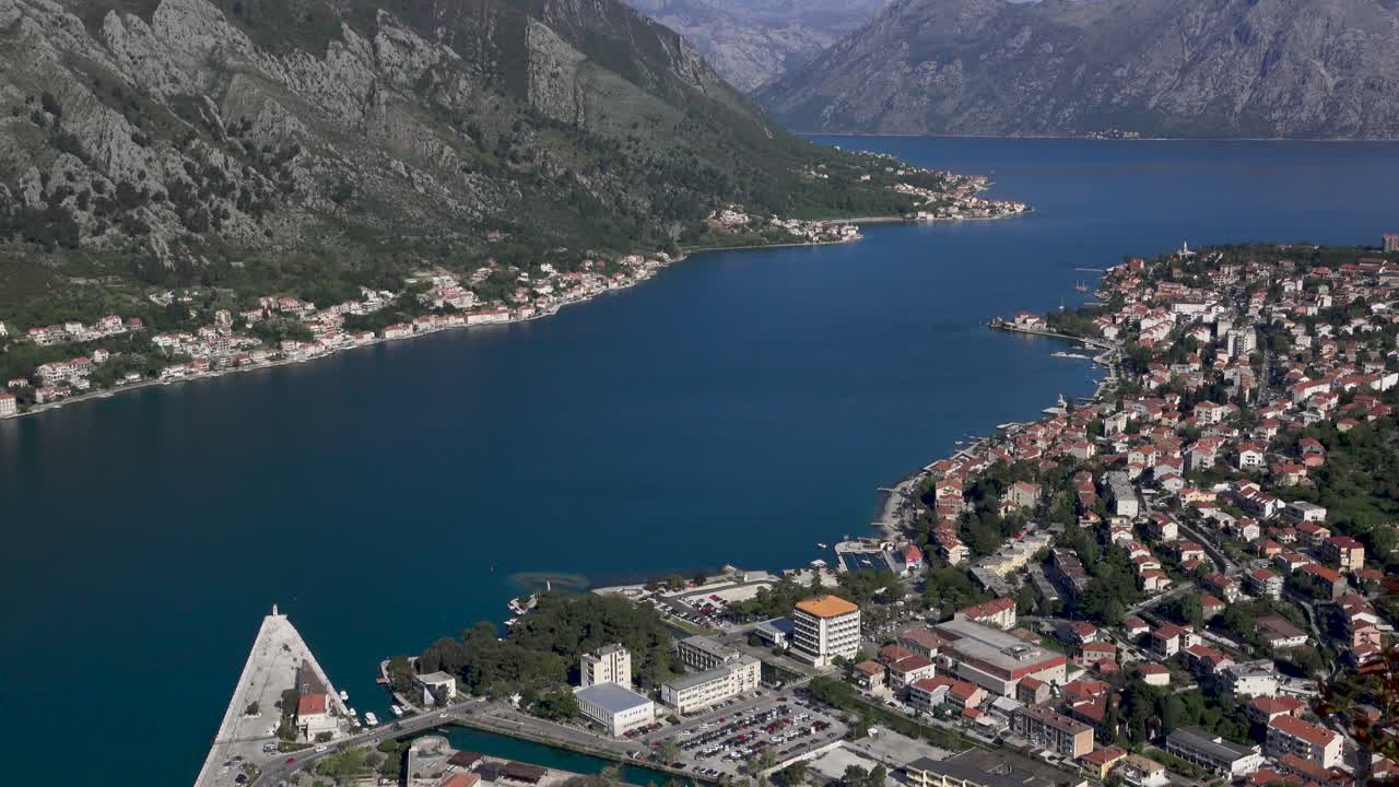 Aerial view of Kotor Bay and the town of Kotor, Montenegro, from San Giovanni Mountain. Bright midday sun, showcasing the city, bay, and surrounding mountains. 4K static footage.