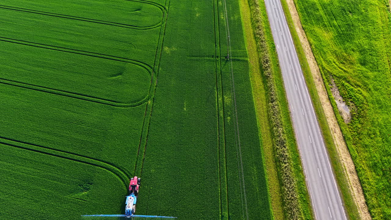 Drone follows tractor sprayer moving through large green field in daylight, agriculture scene