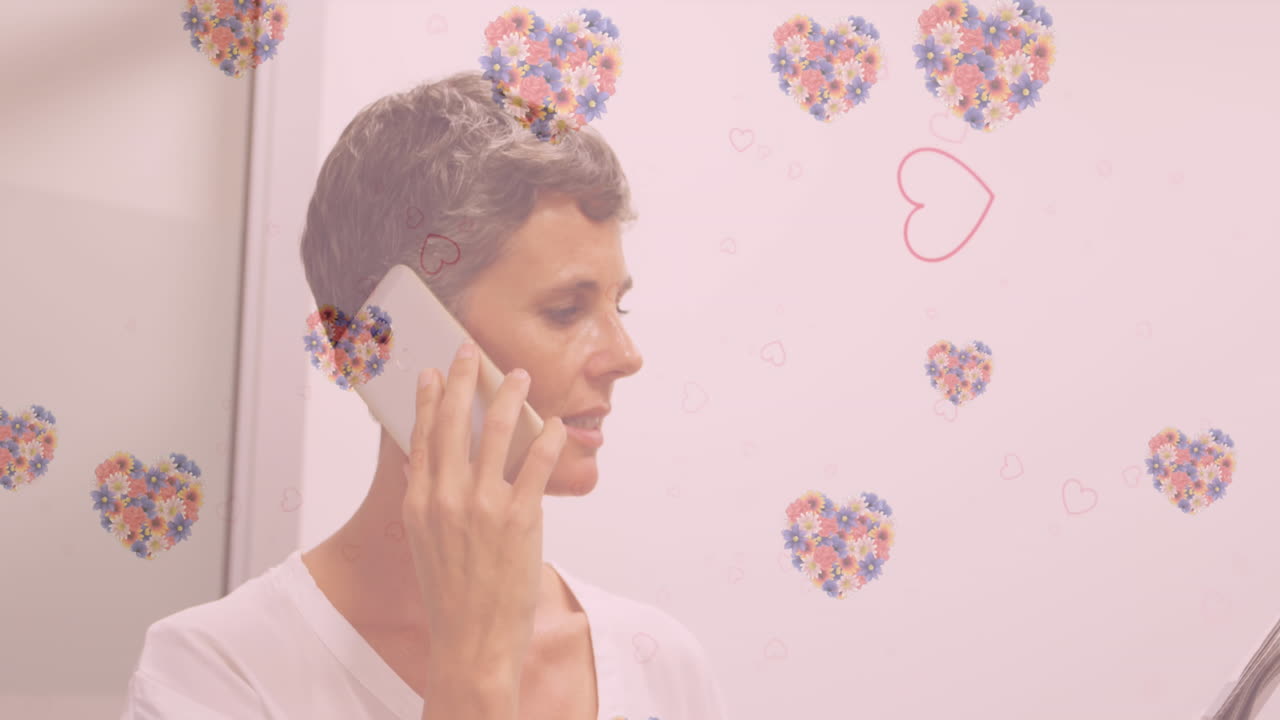 animación de flores en forma de corazón volando sobre mujer caucásica sosteniendo papeles y hablando por teléfono