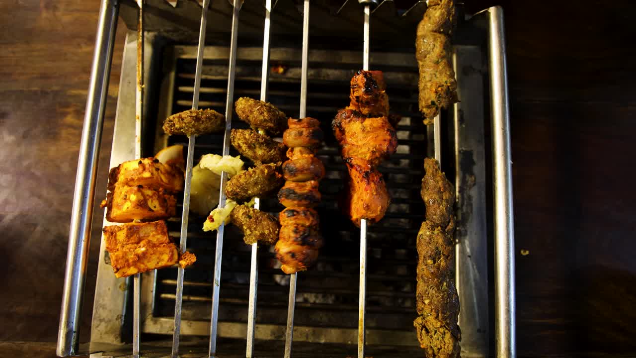 Variety of grilled meat and paneer skewers on open charcoal grill