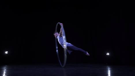 cyr wheel performer shows tricks on a black stage with smoke