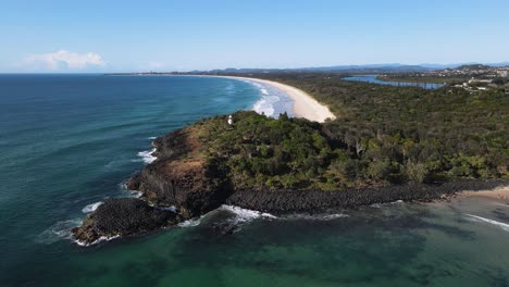 vista panorámica de un faro histórico encaramado en un escarpado promontorio costero rodeado de vegetación autóctona y olas oceánicas