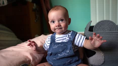 6-month-old baby boy infant in overalls laughing and smiling in nursery