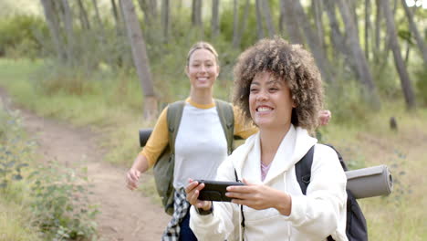 Dos-Mujeres-Disfrutan-De-Una-Caminata-En-Una-Zona-Boscosa,-Una-Con-Un-Teléfono-En-La-Mano.