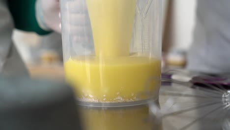 Pouring-natural-oil-mixture-into-a-jar-with-oats-to-create-soap-bars,-Close-up-handheld-shot