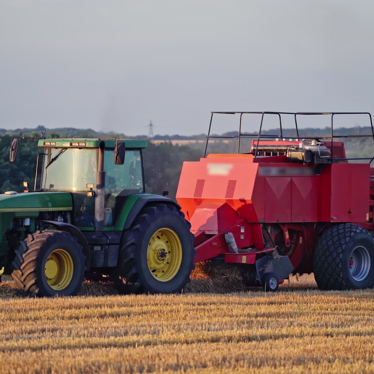 Modern tractor collects dry grass and pressing it into bale. Agricultural process of gathering hay on the golden field. Close-up.