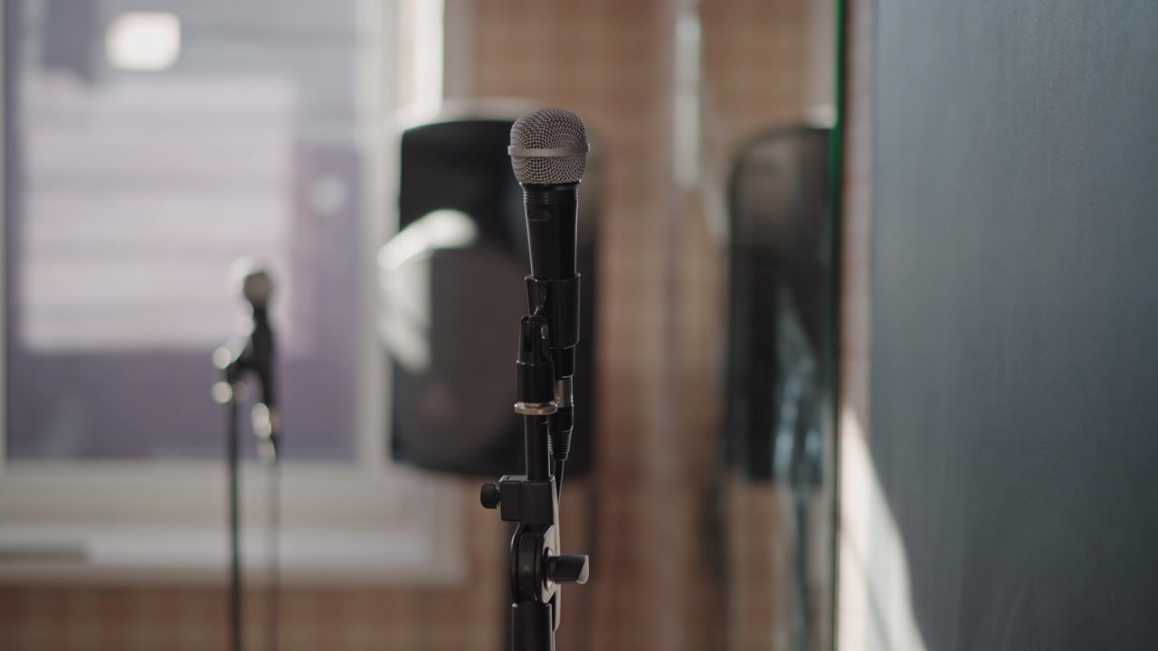 Mid shot microphone in studio, speaker and monitor in background, mixing console out of focus, quiet production vibe, demo recording session, songwriter preparation, mesh detail and warm ambient light