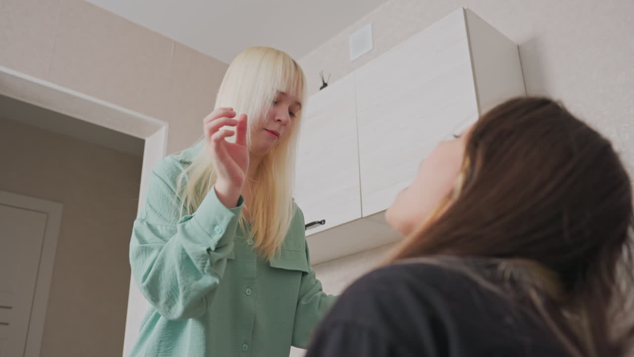 girl opens mouth in playful attempt to catch popcorn tossed by sister in bright home kitchen setting during lighthearted bonding moment filled with laughter fun and cheerful sibling interaction