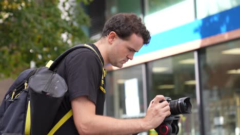 Young-caucasian-man-is-holding-and-adjusting-his-camera-that-is-on-a-tripod